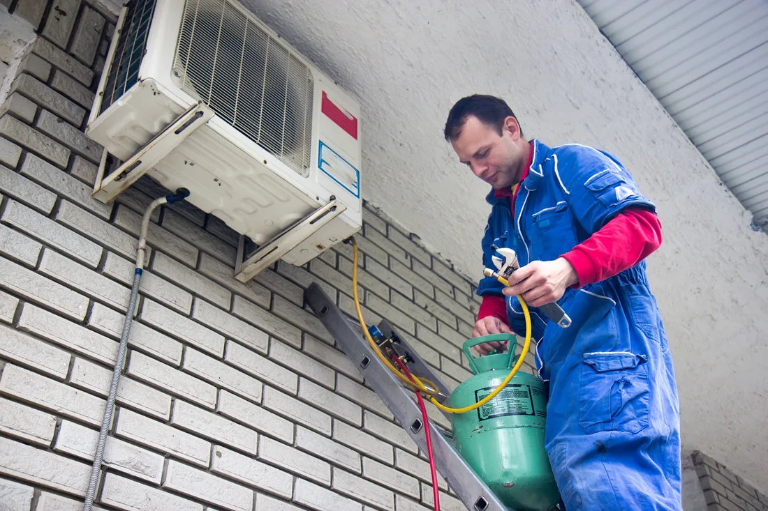 This image depicts a technician working on installing or servicing an air conditioning unit