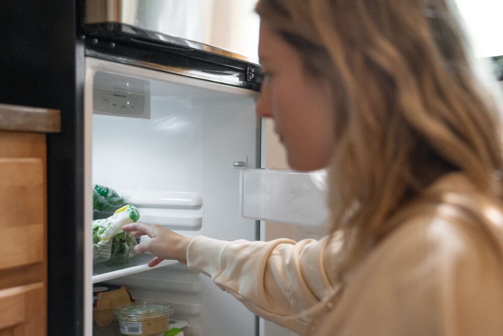 Person reaching into an open refrigerator to place groceries on a shelf.